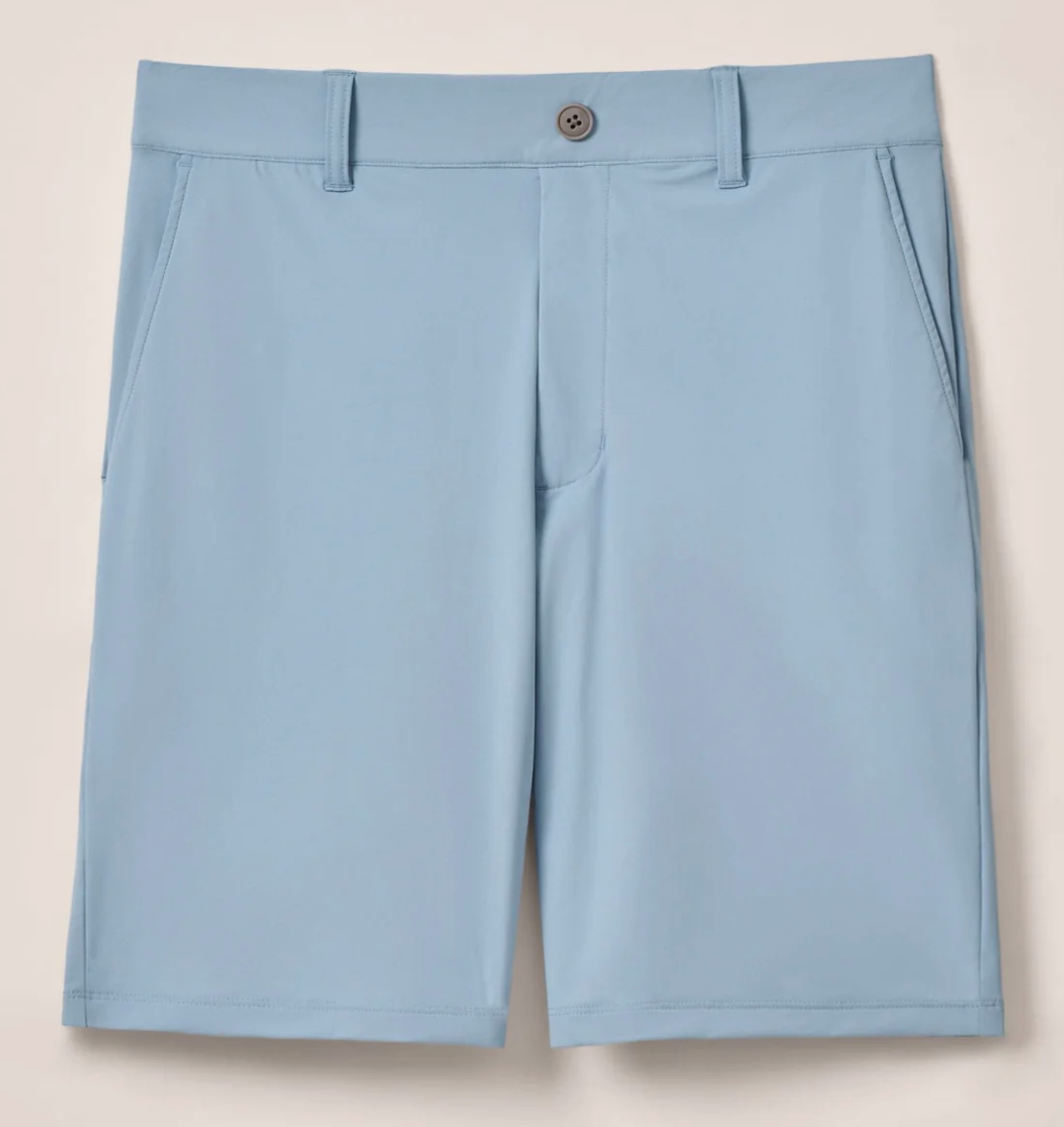 The Johnnie-O Fusionn Short is a light blue men’s performance chino short, crafted from stretch-knit fabric for enhanced comfort. It features side pockets, belt loops, and a front button closure, all showcased against a plain background.