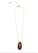 The La Paz Pendant Necklace by Lizzie Fortunato features an oval brown ceramic pendant accented with two vertically set round gemstones—one green, possibly amazonite, and one clear—suspended from a gold-plated chain.