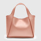 The Stella McCartney Logo Crossbody Tote Bag is a blush pink vegan leather tote with dual top handles and a structured, minimalist design, shown against a plain light gray background.