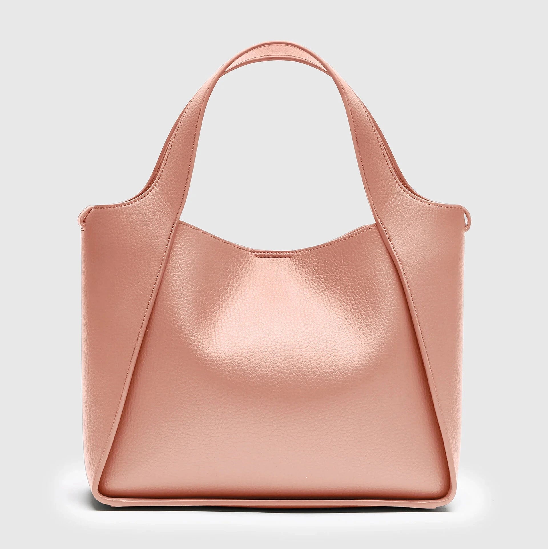The Stella McCartney Logo Crossbody Tote Bag is a blush pink vegan leather tote with dual top handles and a structured, minimalist design, shown against a plain light gray background.