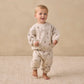 A toddler stands barefoot on a textured beige rug, wearing a matching cream-colored sweatshirt and Quincy Mae Baby Boys’ and Boys’ Oversized Sweatpants featuring a small floral print and an elastic waistband, against a plain beige background.