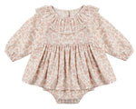 The Quincy Mae Baby Girls’ Thalia Romper features long sleeves, a ruffled collar, and a delicate pastel pink and beige floral pattern with charming embroidery, showcased against a plain white background.
