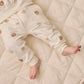 A baby lies on a cream-colored quilt, wearing Quincy Mae Baby Boys’ and Boys’ Relaxed Fleece Sweatpant featuring a cozy bear face pattern. With only the legs and lower torso visible, these sweatpants are an ideal choice for everyday comfort.