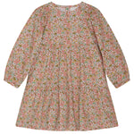 The Girls’ Puff Dress by Serendipity is a long-sleeved, knee-length organic cotton dress adorned with a hand-drawn flower print in pink, green, and white. It features a round neckline, subtle puff sleeves, and a loose, tiered silhouette.