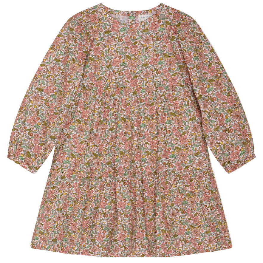 The Girls’ Puff Dress by Serendipity is a long-sleeved, knee-length organic cotton dress adorned with a hand-drawn flower print in pink, green, and white. It features a round neckline, subtle puff sleeves, and a loose, tiered silhouette.
