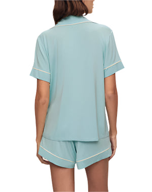 Wearing the Eberjey Gisele Relaxed Short PJ Set in light blue with white trim, a person enjoys a comfortable fit with a short-sleeved top and shorts. A functional pocket elegantly enhances the design as they face away.