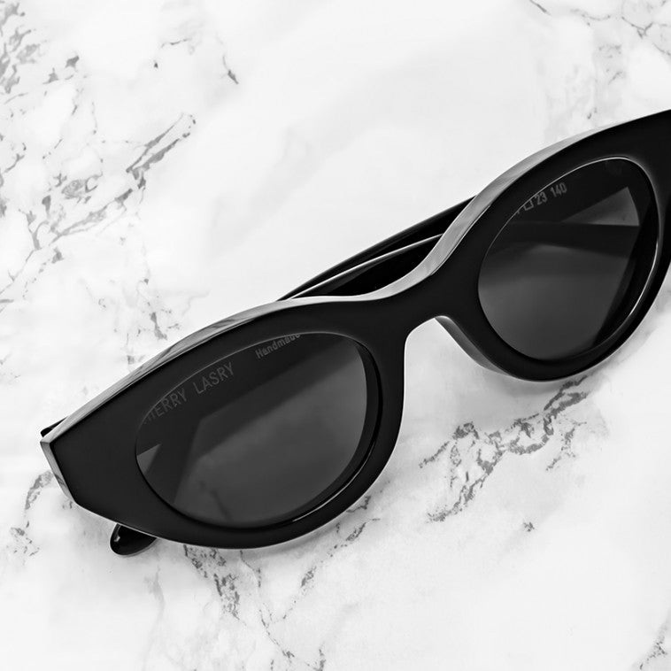 Expertly crafted in France, the Thierry Lasry Acidity Sunglasses by Thierry Lasry feature a stylish black cat-eye design and rest elegantly on a white marble surface, offering chic style with UV protection.