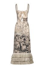 The Invictus Ankle Dress by Johanna Ortiz features braided straps, a front bow tie, and a tropical botanical print, accented with layered fringe trim at the hem for added movement.