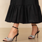 Woman wearing a long black skirt and Loeffler Randall Ada Black Knot Heeled Sandals with adjustable buckle ankle strap.