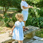A boy wearing Kidiwi's Baby Boys' and Boys' Adam Shorts stands on a stone bench holding greenery, while a girl in a blue dress stands beside him in a garden setting.