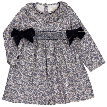 The Kidiwi Baby Girls' and Girls' Adriana Corduroy Bows Smocked Dress features a blue and white floral pattern, handmade smocking on the chest, and two black velvet bows at the waist for a charming look.