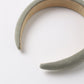 A close-up of the Rylee & Cru Girls’ Padded Headband, featuring a stylish, fabric-covered design in a light grayish-green color, displayed against a white background.