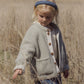A young blonde-haired child with a blue headband stands in a dry field, gently touching tall grass while wearing the Rylee & Cru Baby Girls’ and Girls’ Chalet Jacket, featuring a cozy sherpa design and quilted button placket.