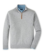 The Peter Millar Artisan Crafted Cashmere Flex Quarter-Zip in light gray features a brown zipper pull and is worn over a blue collared shirt, drawing inspiration from classic British knitwear.