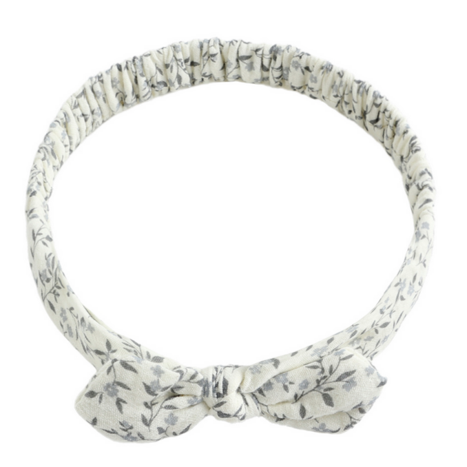 The Rylee & Cru Baby Bow Headband features a soft white band with a gray leaf pattern, a small bow, and a comfy scrunchy elastic back for babies.