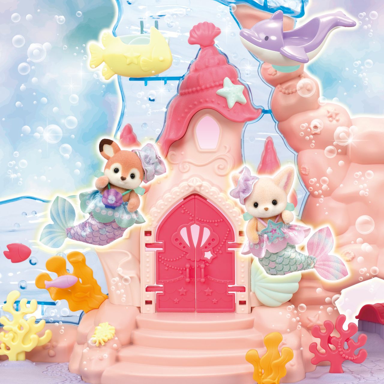 Two Calico Critters Baby Mermaid Castle figures with mermaid tails sit in front of the whimsical castle door, surrounded by colorful coral and sea creatures, set against an underwater-themed background filled with bubbles.