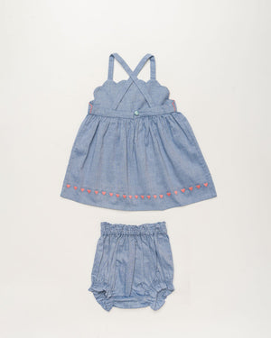 The Early Sunday Baby Girls’ Alice Baby Dress & Bloomer Set features a sleeveless blue cotton chambray dress with crisscross straps and adorable pink heart accents, paired with coordinating blue bloomers—evoking the charm of a summer sky, all showcased on a simple white background.