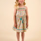 A young girl with blonde hair stands facing forward in the Early Sunday Girls’ Alisson Dress, crafted from organic cotton with a mint floral pattern, paired with beige shoes against a plain, light beige background.