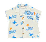 The Arsene & Les Pipelettes Baby Boys' Collared Shirt is a short-sleeved white shirt decorated with blue waves, blue plants, orange dots, and a printed "A.P". It features a classic collar, chest pocket, and brown buttons down the front for an added touch of style.