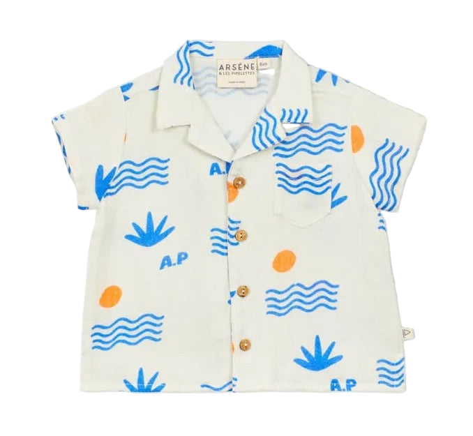 The Arsene & Les Pipelettes Baby Boys' Collared Shirt is a short-sleeved white shirt decorated with blue waves, blue plants, orange dots, and a printed "A.P". It features a classic collar, chest pocket, and brown buttons down the front for an added touch of style.