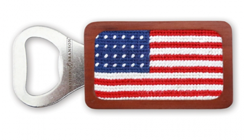 The Navy American Flag Bottle Opener by Smathers & Branson features a chestnut-colored wood handle with an embroidered American flag design, highlighting the charm of needlepoint craftsmanship.