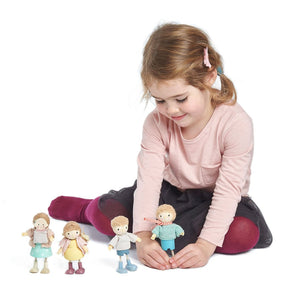 A young girl in a pink shirt and dark skirt sits on the floor, playing with Tender Leaf Toys' "Amy & Her Rabbit" solid wood doll figures arranged before her on a white background.