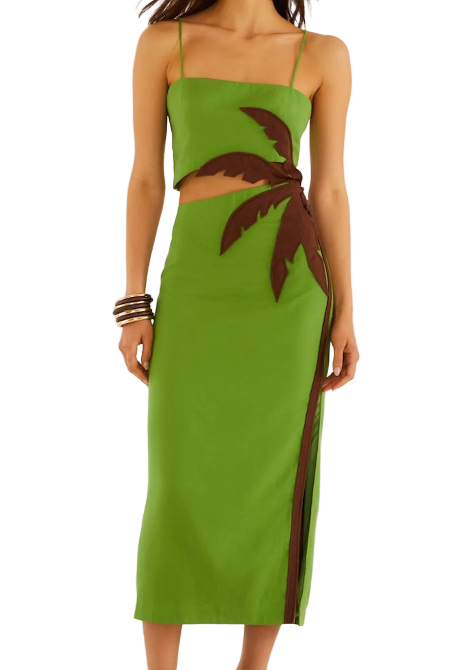 A woman wears the Green Palm Tree Maxi Dress by Farm Rio, a two-piece outfit with a brown palm tree design on the skirt and bangles on one arm.