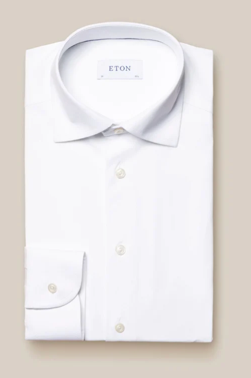 The Eton Four-Way Stretch Shirt, Slim Fit, in white tech fabric features a classic collar and buttoned cuffs. A visible Eton label accents its neatly folded display on a beige background, highlighting exceptional comfort.
