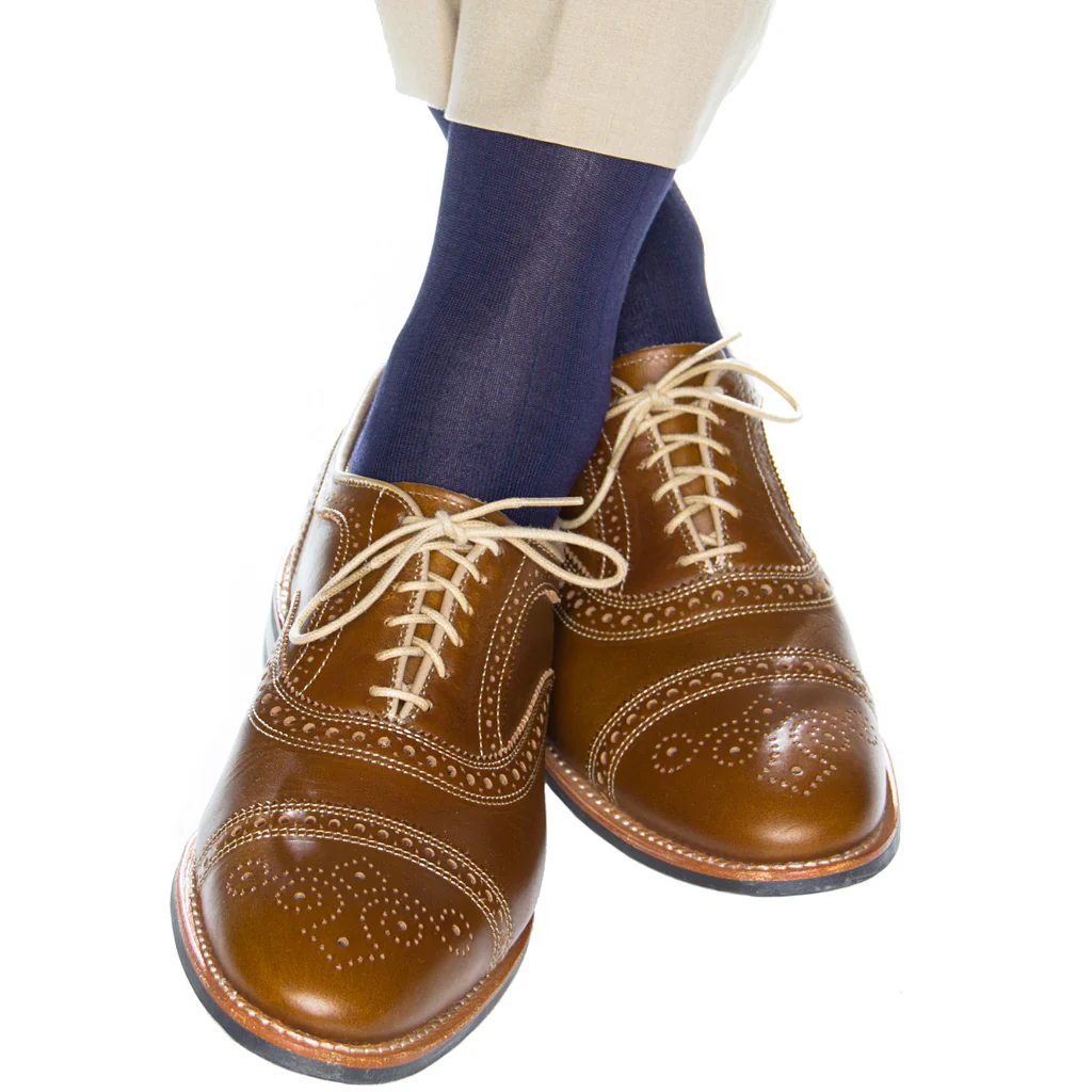 A person wearing light brown oxford dress shoes, beige pants, and Dapper Classics Classic Navy Ribbed Mid Calf Socks, with their legs crossed on a white background.