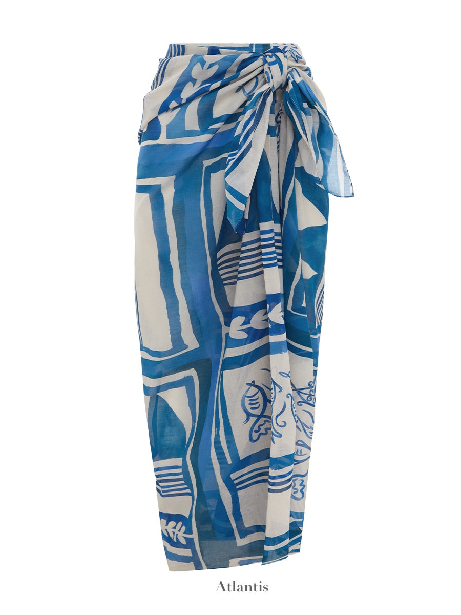 A stylish square pareo made of organic cotton, featuring abstract and floral patterns in blue and white with a knot at the waist. The words "Soleil Soleil" are written below the image. This chic beach cover-up is known as the Soleil Soleil Square Pareo.