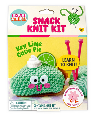 The Snack Knit Kit - Key Lime Pie by Bright Stripes features a cheerful green knitted pie slice with a smile, topped with whipped cream and a lime, plus knitting needles. The packaging includes the phrases "Key Lime Cutie Pie," "Learn to Knit!" and "Ages 8+." Ideal for beginner knitters, this charming craft kit makes learning to knit easy—and deliciously cute!.