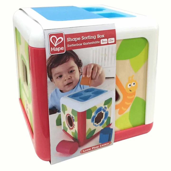 A box displays a young child playing with the Hape Shape Sorting Box, a colorful wooden toy featuring shapes and a worm illustration—an engaging educational toy for toddlers.