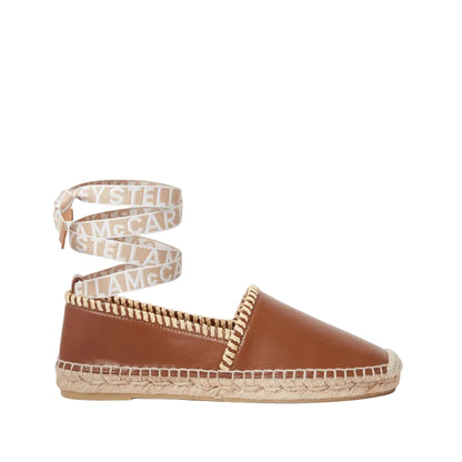 The Gaia Whipstitched Flat by Stella McCartney features a tan leather upper, beige ankle tie with logo, woven sole, and handcrafted details that highlight natural textures.