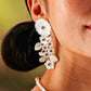 A close-up of a person wearing Juliska Capucine De Wulf's Mermaid Garden Convertible Statement Earrings, featuring mother of pearl white flowers, leaf designs, and gold and turquoise accents.