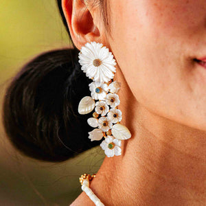 A close-up of a person wearing Juliska Capucine De Wulf's Mermaid Garden Convertible Statement Earrings, featuring mother of pearl white flowers, leaf designs, and gold and turquoise accents.