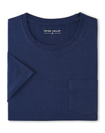 A folded navy blue Crown Comfort Short-Sleeve Pocket Tee by Peter Millar is displayed, crafted from soft midweight organic cotton with a chest pocket and a visible "Peter Millar" label inside the collar. This tee combines everyday comfort and style.
