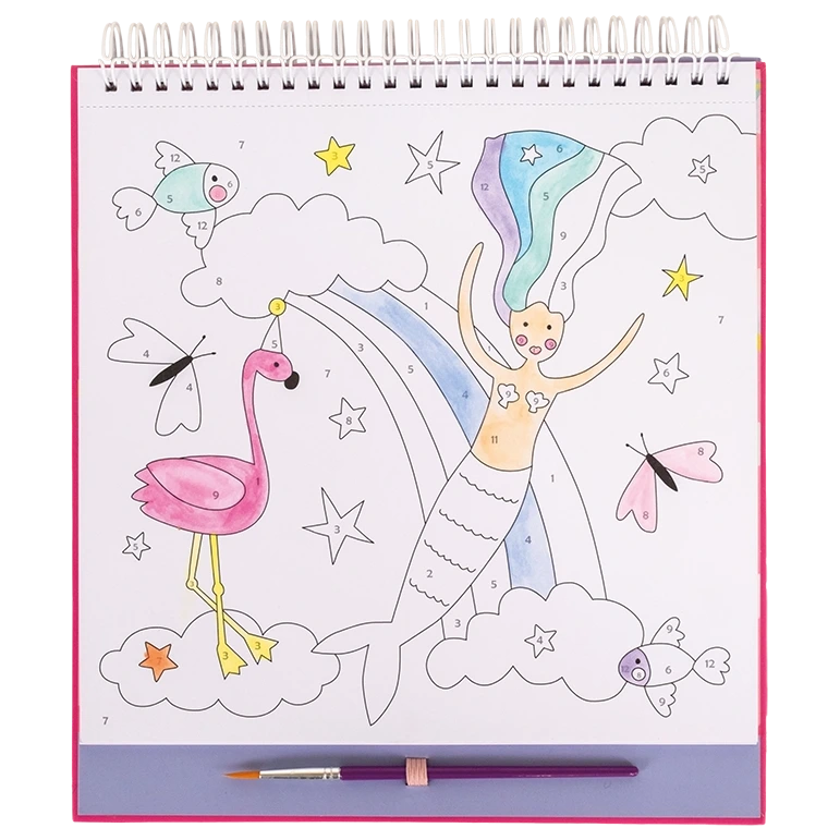 A color-by-number page from the Floss and Rock Fantasy Paint By Numbers kids art kit shows a mermaid, rainbow, clouds, stars, fish, butterflies, and a flamingo. The spiral-bound page is partially colored with a paintbrush resting below it.