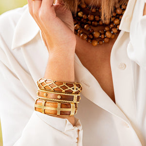 A person in a white shirt wears the Juliska Capucine De Wulf Earth Goddess Hinged Bangle, several wooden bangles, and a brown beaded necklace.