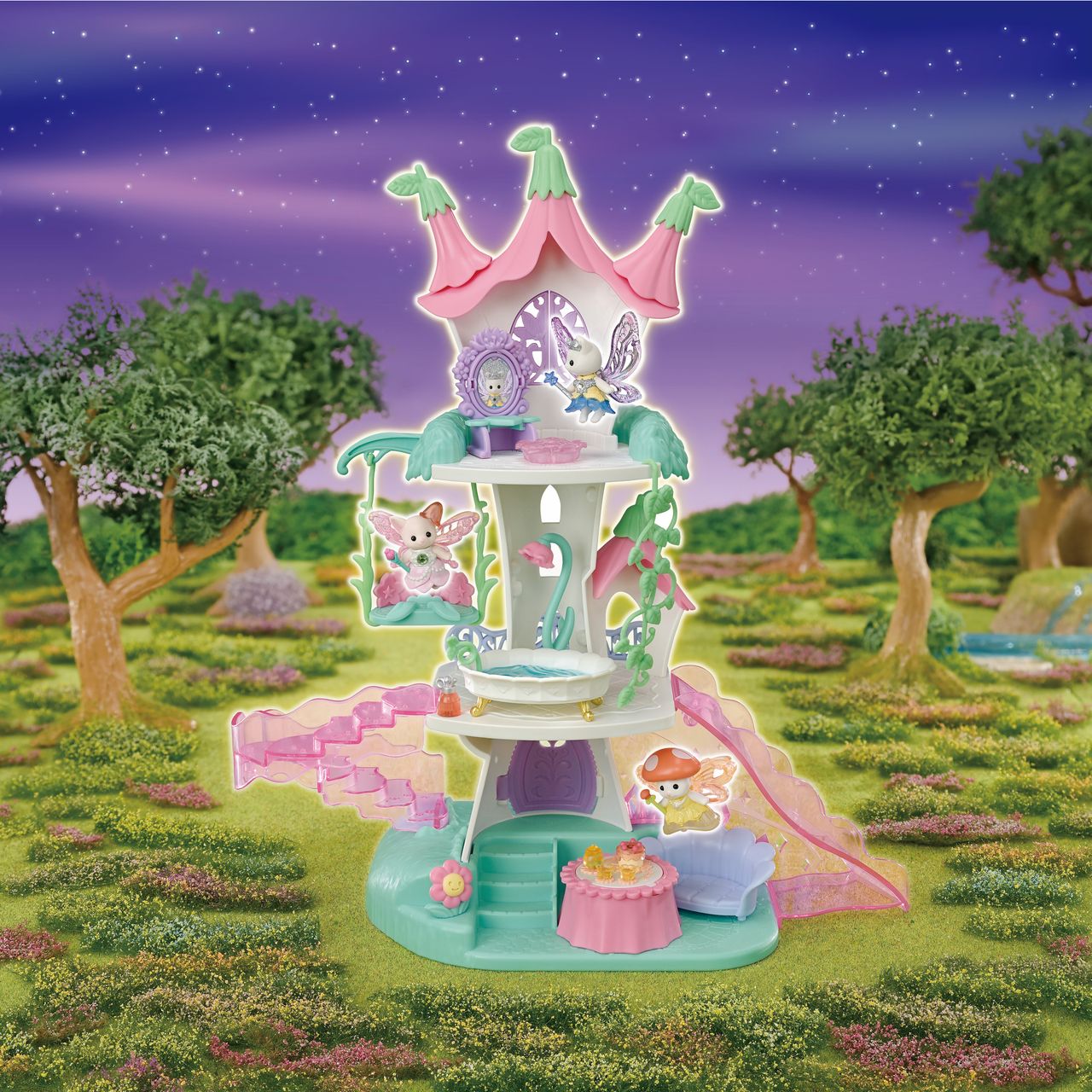 The three-story pastel Fairytale Tower by Calico Critters features adorable Nectar Fairy figures, pink staircases, flower-themed furniture, and whimsical decorations, set outdoors on a grassy landscape with trees beneath a purple night sky.