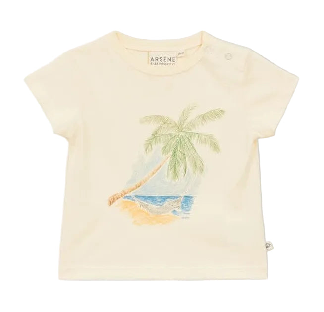 The Arsene & Les Pipelettes Baby Palmier Baby T-Shirt is a cream-colored cotton tee featuring a breathable beach print with a palm tree, sandy shore, and blue ocean, plus two small buttons on the left shoulder.