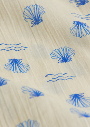 Close-up of cream-colored fabric from the Arsene & Les Pipelettes Baby Girls' Felixia Top, showcasing blue embroidered seashells and wavy lines.