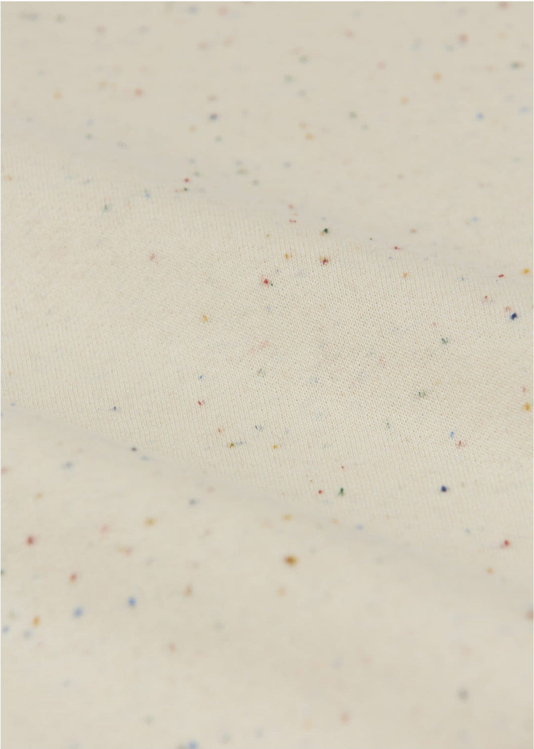 Close-up of cream-colored fabric with multicolored specks and gentle folds, showcasing the soft texture of Arsene & Les Pipelettes Baby Gabano Speckled Joggers.