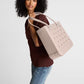 A woman wearing a brown top and jeans carries the Baby Bogg® Bag by Bogg Bags—a large, durable tote with perforated holes and a textured bottom—over her shoulder, making for a stylish, washable carryall that’s perfect for daily errands.