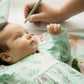 A gender neutral baby is laying on a bed while a woman writes in a notebook, capturing memories for their Write To Me Baby Journal Birth to Five Years Pink.