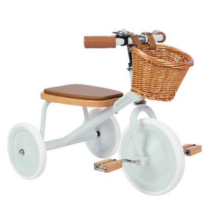 The Banwood Kids’ Trike is a charming children’s tricycle featuring a lightweight frame, white wheels, a brown seat, and an adorable wicker basket attached to the handlebars.