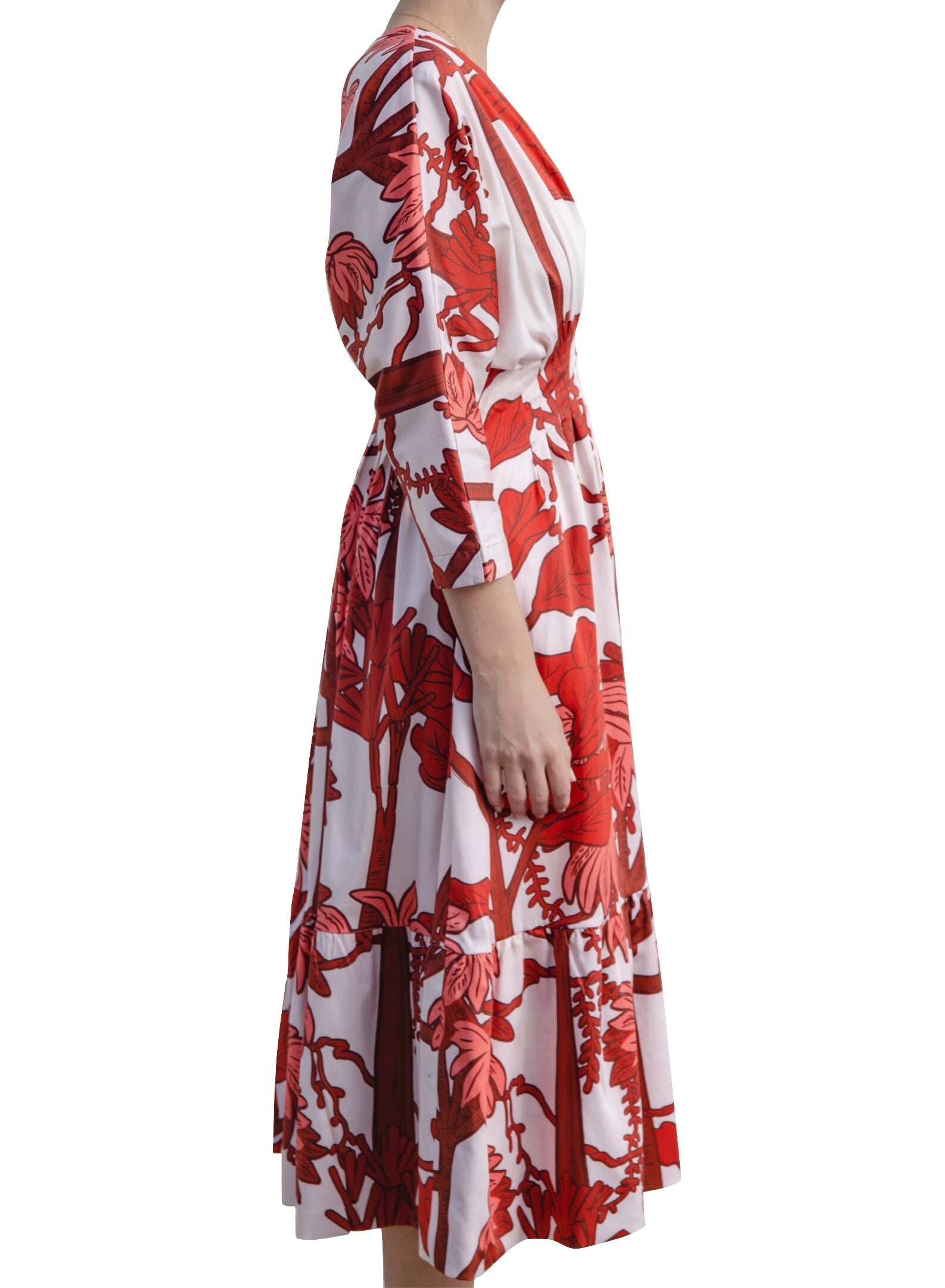 Person wearing an Andres Otalora Batea Dress with a red floral print, made from cotton poplin, shown in a side profile with a graceful V-neckline.