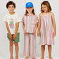 Three children stand barefoot against a white background, with one wearing the Arsene & Les Pipelettes Girls' Bayadere Striped Strap Dress—a breezy summer dress crafted from soft cotton voile in colorful stripes.