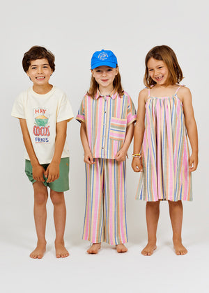 Three children stand barefoot against a white background, with one wearing the Arsene & Les Pipelettes Girls' Bayadere Striped Strap Dress—a breezy summer dress crafted from soft cotton voile in colorful stripes.
