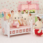 Three Calico Critters plush bunny toys sit and stand around the Crib with Mobile, which features a white frame and a pink mattress, in a pastel-themed dollhouse nursery—an adorable baby nursery set perfect for enhancing any collection of dollhouse furniture.