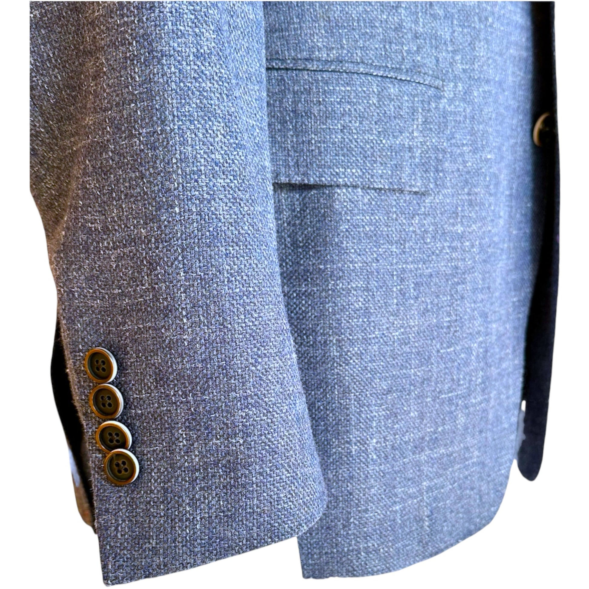 Close-up of the Bennet Natural Chambray Blazer by Samuelsohn shows a gray textured sleeve with four brown buttons and a pocket, highlighting the refined craftsmanship typical of luxury menswear and custom tailoring.
